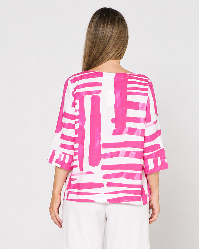 A woman viewed from the back wearing a bright pink and white abstract patterned top with three-quarter ruffled sleeves, paired with white wide-leg cropped pants and brown block-heel sandals, against a plain white studio background.