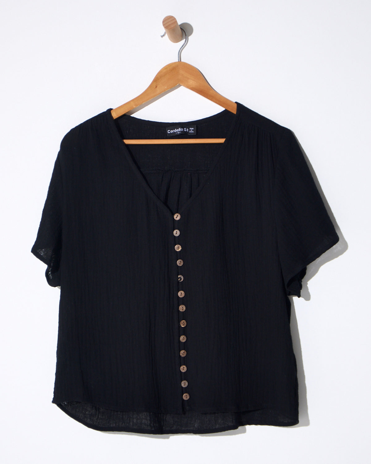Tarin Button Top in black, on a hanger showing the button front and short sleeves