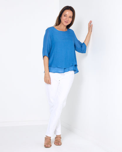 Leo Layered Top in denim blue, full-length view styled with white pants and sandals