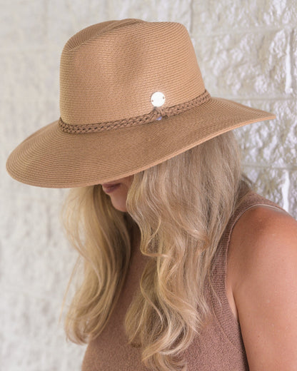 Person wearing a brown straw hat with a decorative band against a textured white wall.