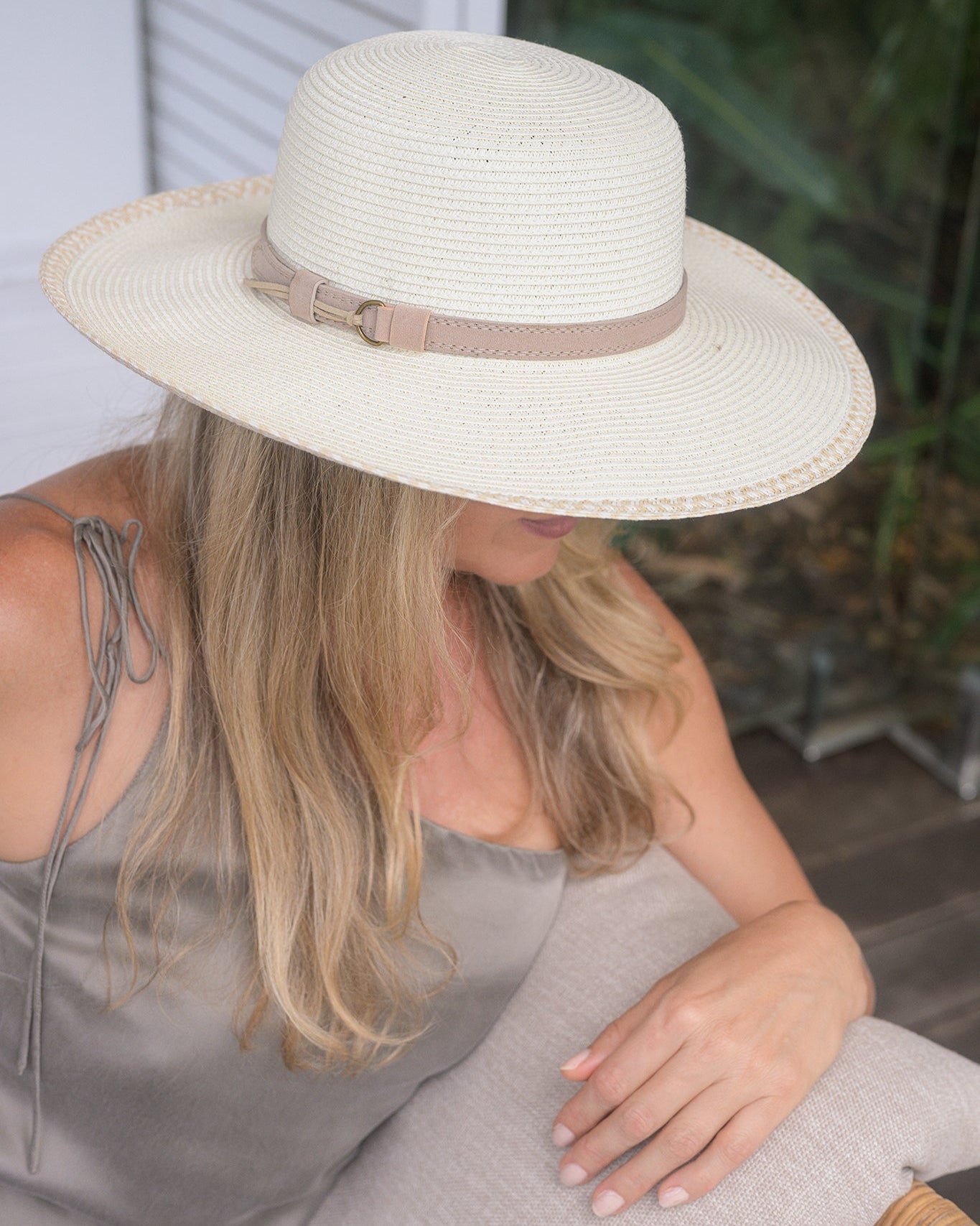 Woman wearing a white straw hat with a brown band, sitting on a wooden bench.
