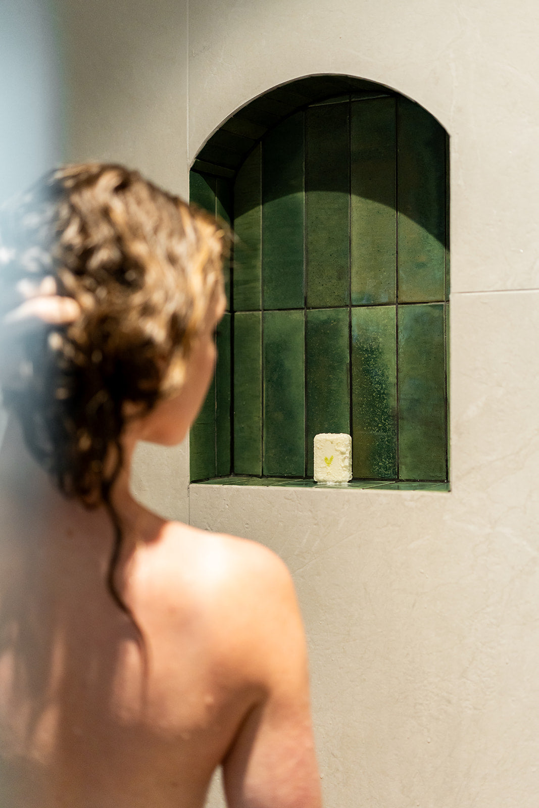 Person standing in a shower with green tiled niche on the wall.