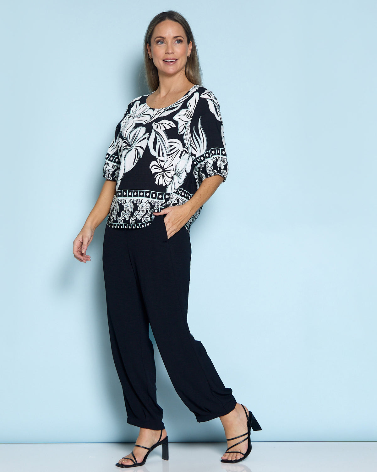 Falkiner Border Print Top in black, full-length view against a blue backdrop, worn with black pants