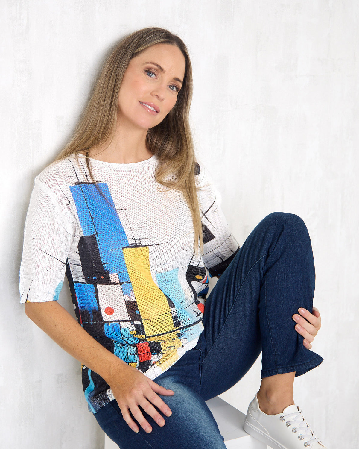 Caprina Knit Top in colour blocks, seated view styled with dark jeans and white sneakers